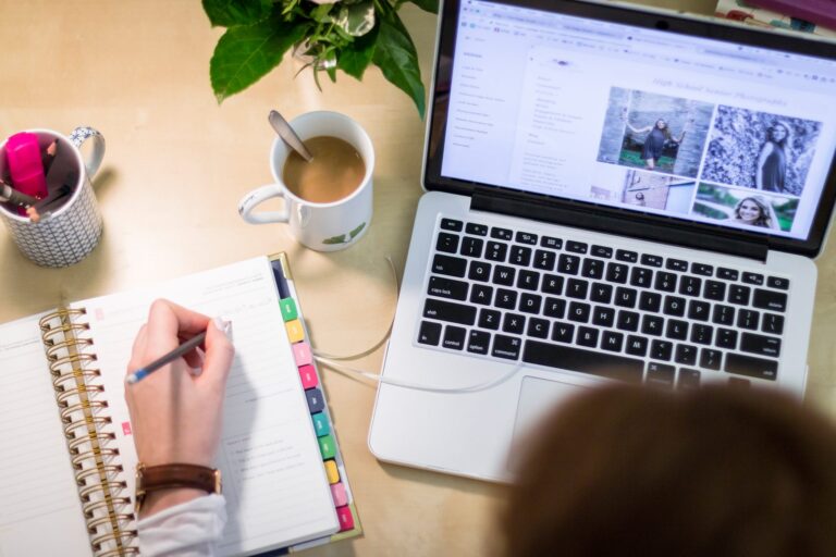 Aerial view of a woman writing in a planner with an open laptop and a cup of coffee