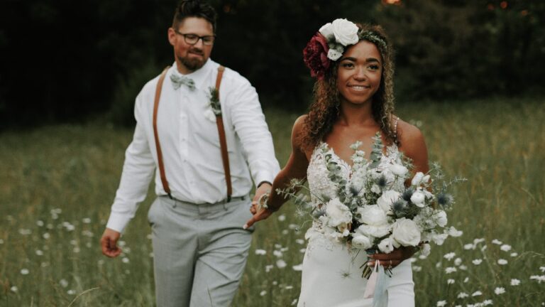 married couple in a field, holding hands and looking past the camera