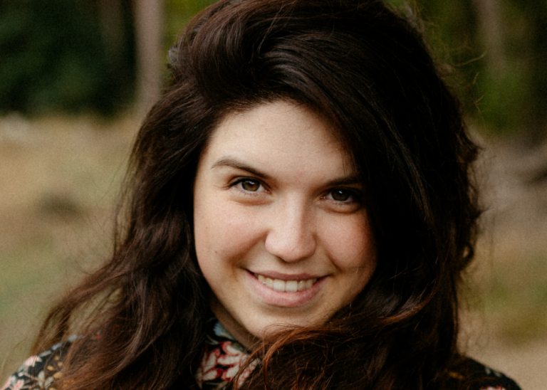 Close up of a woman outside, smiling at the camera.