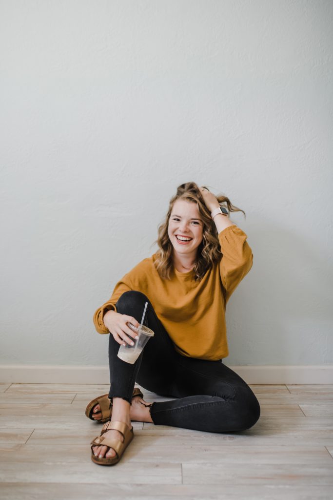 a woman sitting on the floor holding a to go drink with a straw