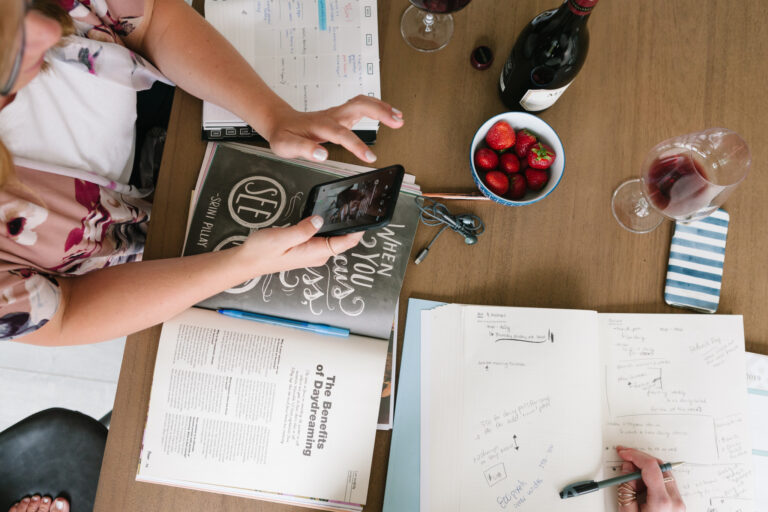 Aerial view of two people working at a table with wine, strawberries, and an assortment of papers.