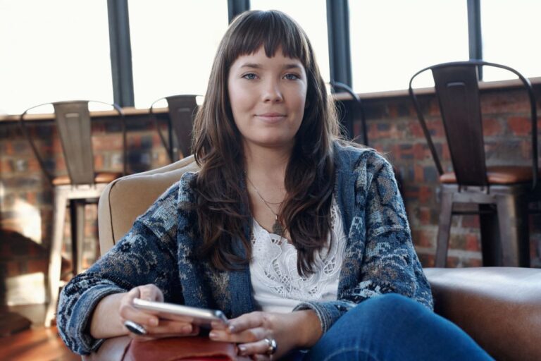 Woman with long brown hair smiles while holding phone.