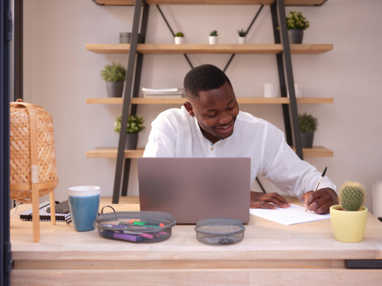 One Black delighted businessman in white shirt taking notes on paper sitting in modern office at his desk.