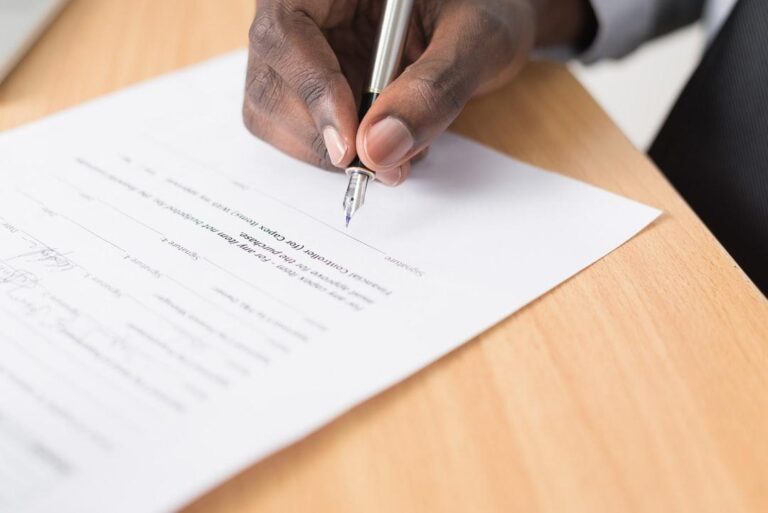 Close-up of a person signing a legal contract with a pen on a wooden desk